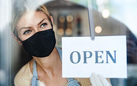 Store owner wearing mask looking out window as she opens store