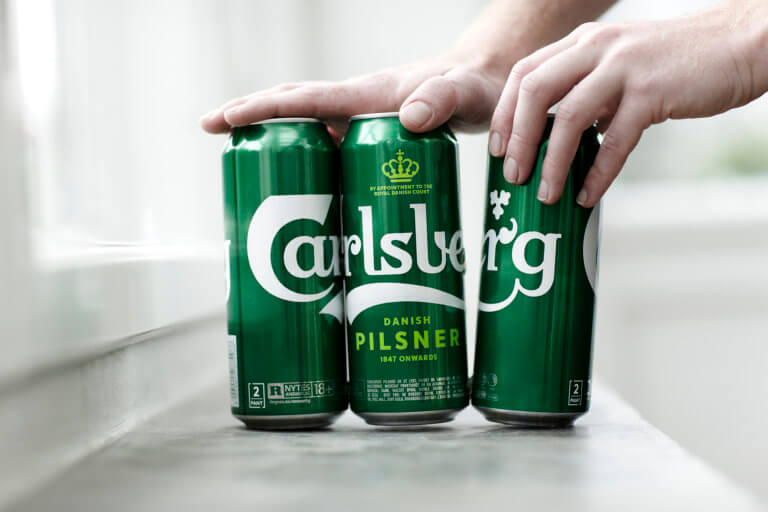 a six pack of Carlsberg beer with one can being pulled out by a hand