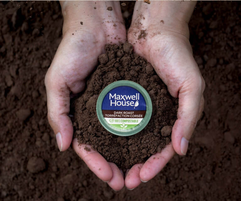 Maxwell house zero waste coffee pod held in a persons hand surrounded by dirt