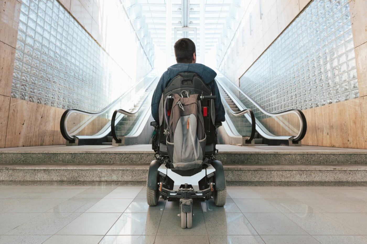 person in wheelchair looking up at inaccessible entranceway with stairs